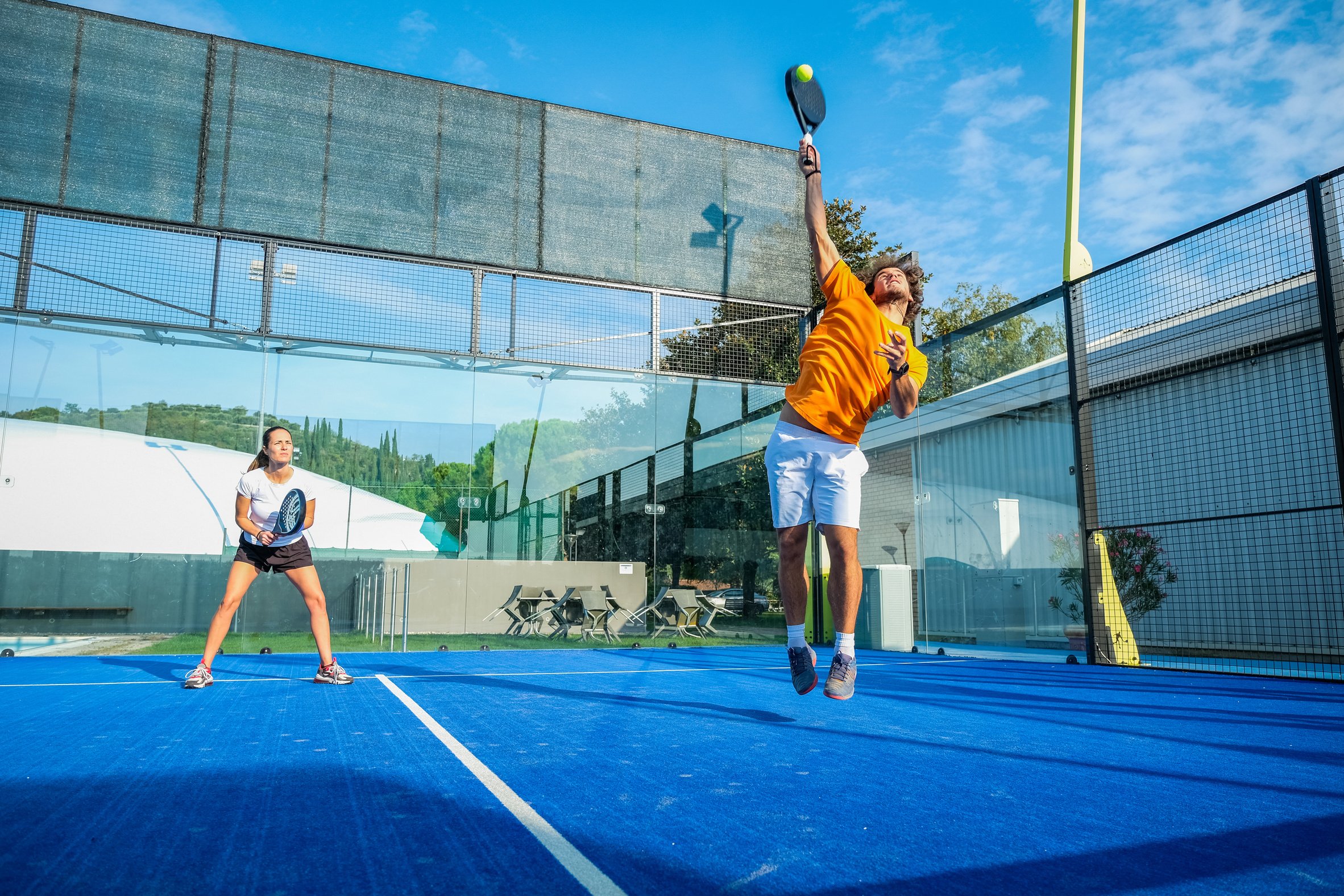 Mixed padel match in a blue grass padel court -  Beautiful girl and handsome man playing padel outdoor